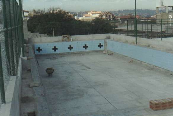 Imagem da piscina do Colégio sendo construída, com azulejos apenas nas laterais e sem água