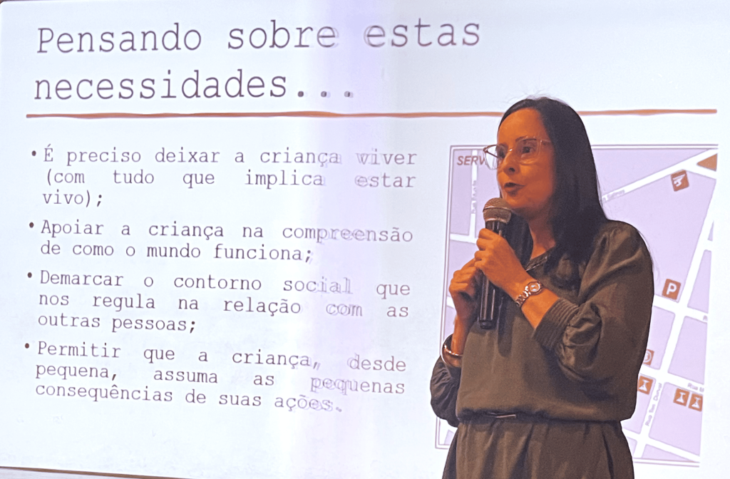 Profa. Catarina de óculos, com microfone nas mãos, fala sobre o desenvolvimento gradual da moralidade
