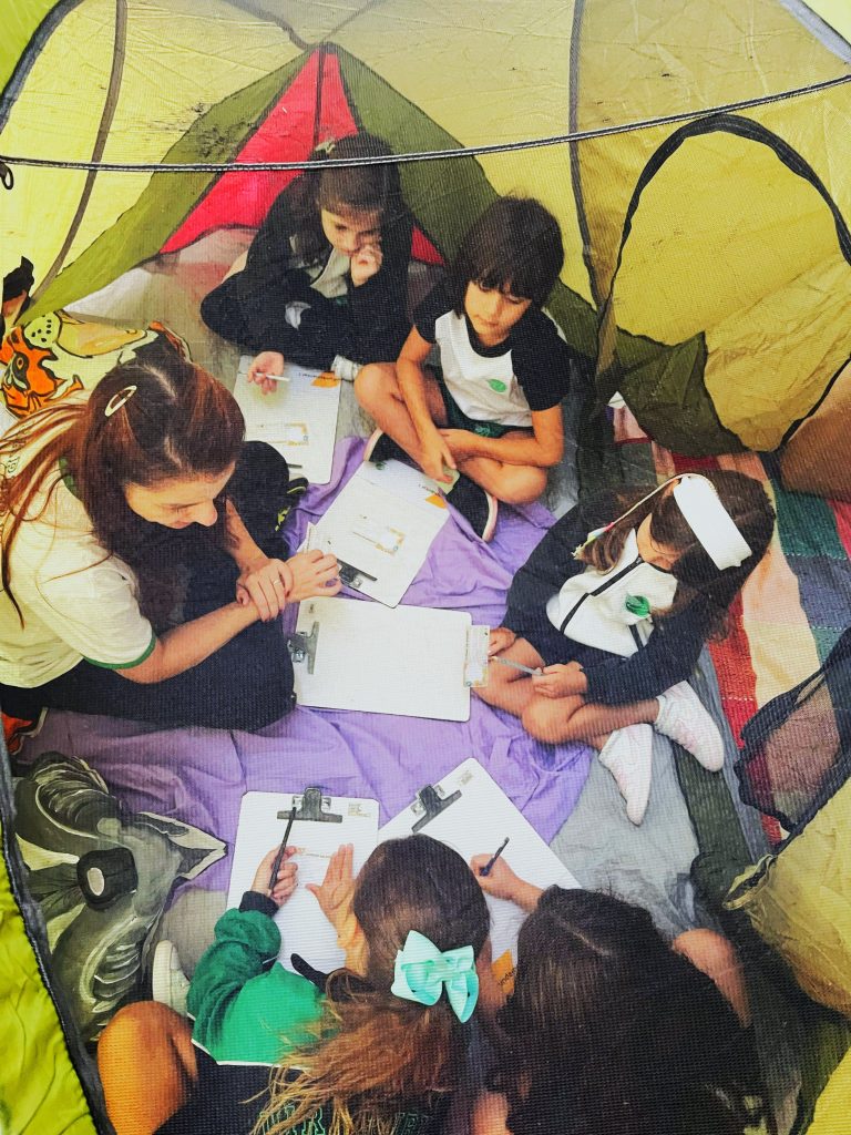 Crianças com professora sentadas em círculo dentro de barraca, no Clubinho das emoções